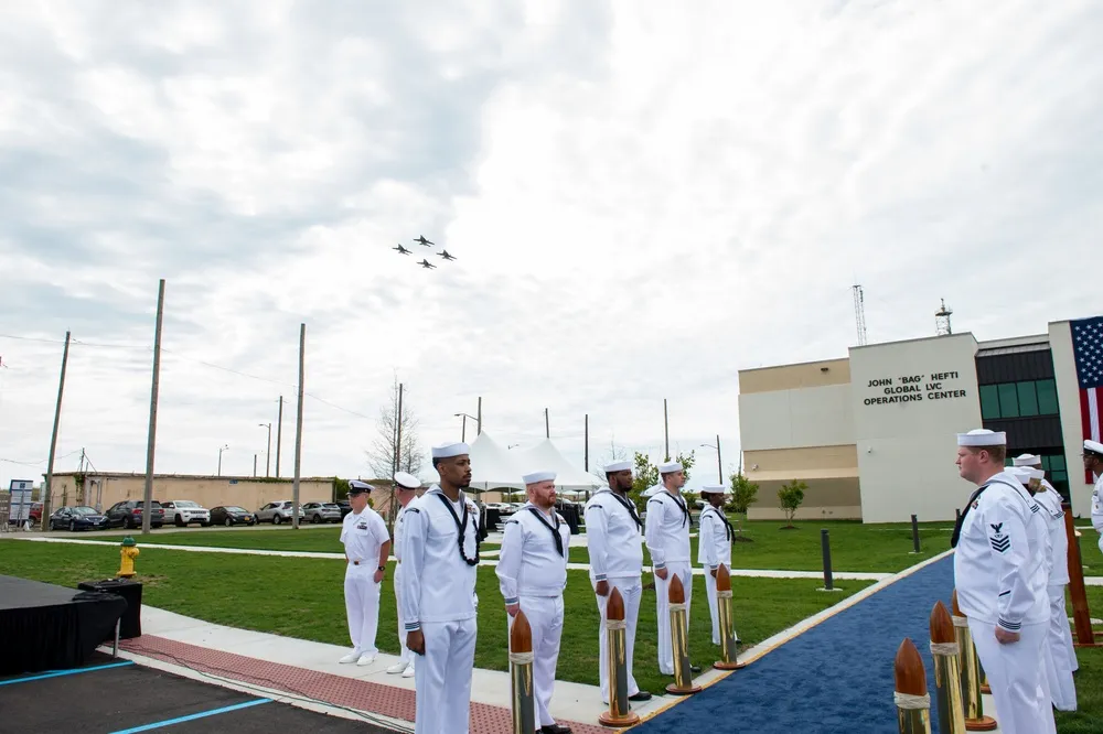Sailors stand at attention as fighter jets fly over the Hefti Global LVC Operations Center